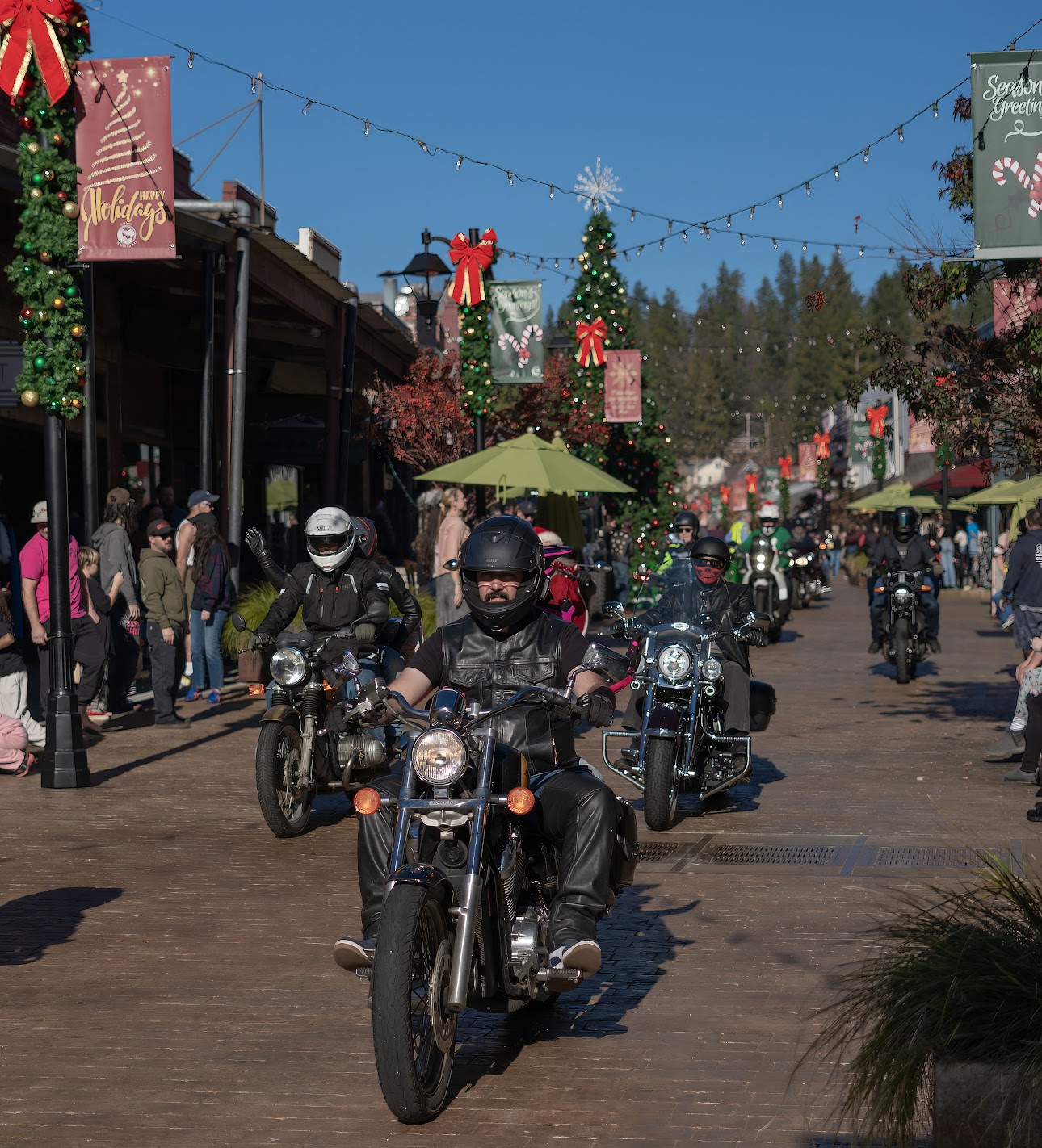 Motorcycle riders passing through downtown during the Nevada County Toy Run, with Christmas decorations and spectators lining the street.