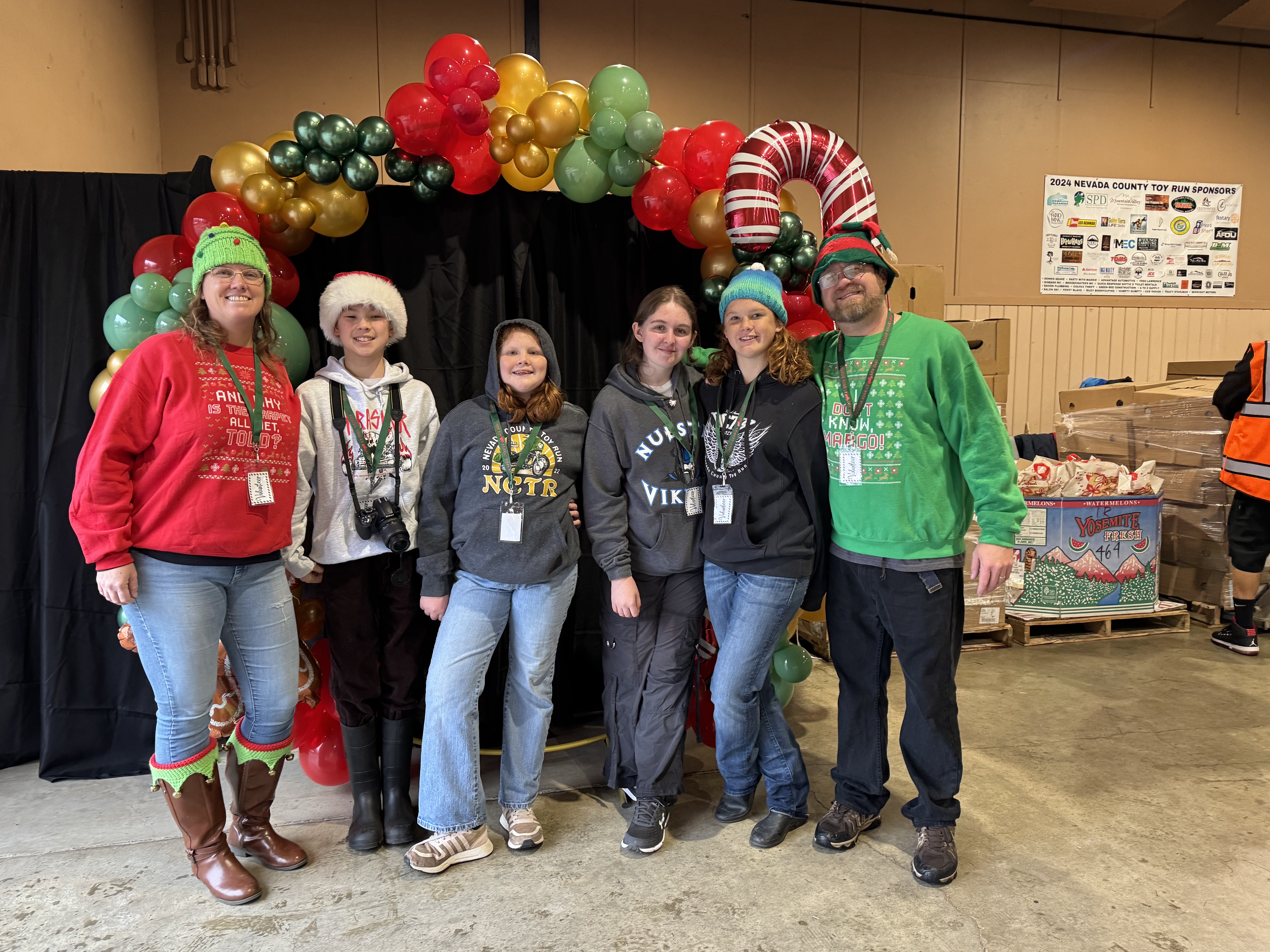 Toy Run volunteers in festive clothing gathered beneath a Christmas balloon arch.