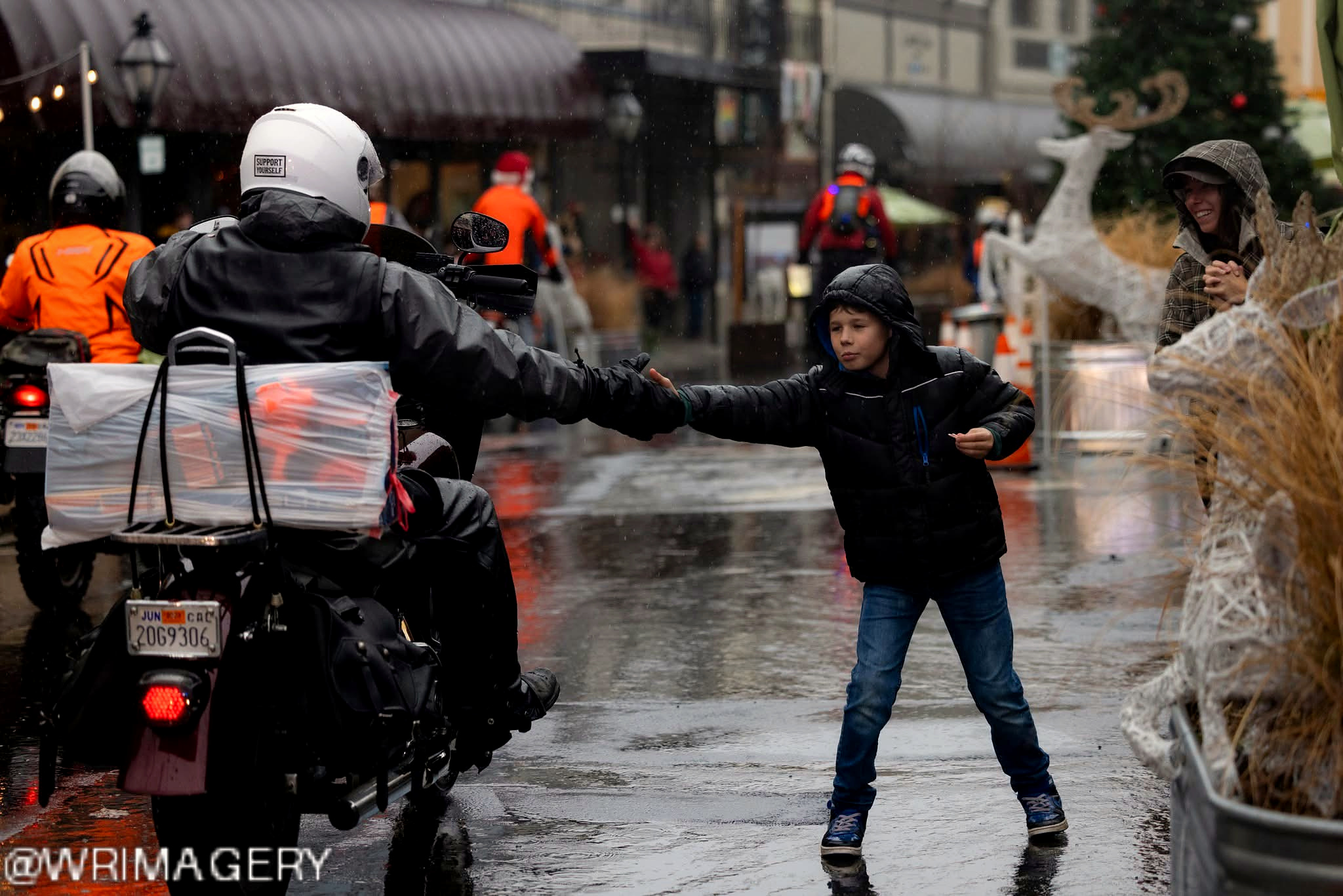 A motorcycle rider greeting a child along the rainy Toy Run route.